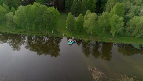 small boats moored at the pier by the lake where families and people spend their free time at village fun in the middle of a natural spring landscape with trees