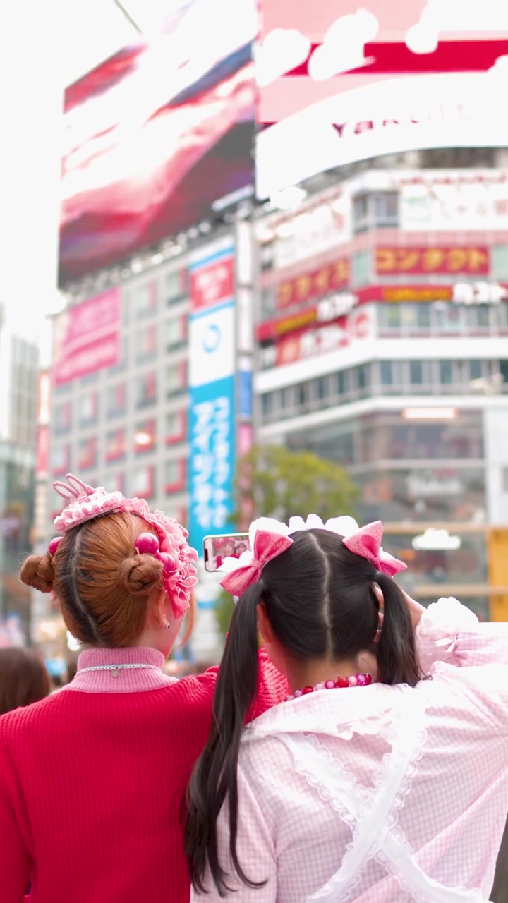 Due ragazze che indossano abiti colorati in stile decora camminano per una trafficata strada di Tokyo con cartelloni pubblicitari urbani.