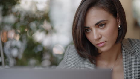 una mujer hispana está sentada en una silla y escribiendo o tomando notas mientras asiste a una clase de video en línea o a una reunión de oficina en una computadora portátil.