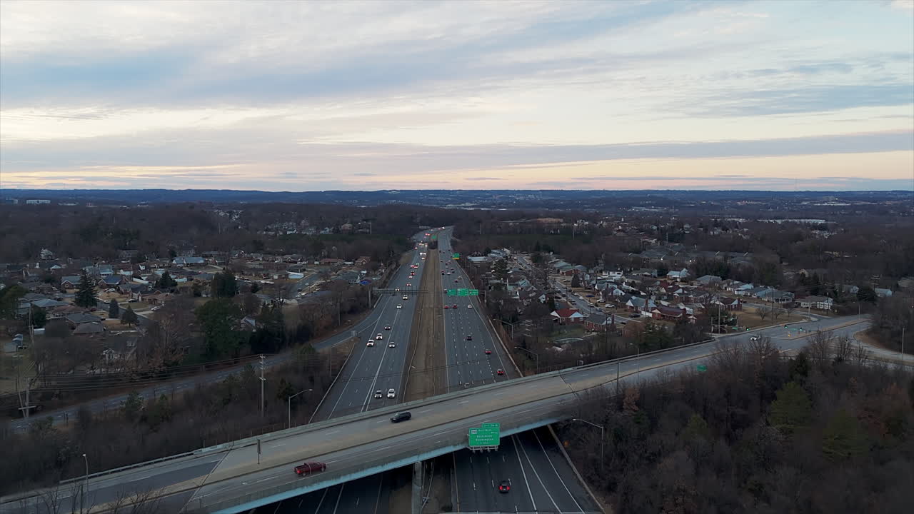 Traffic On Highways At Dusk, Surrounded By Leafless Trees And Suburban Homes. aerial pullback shot