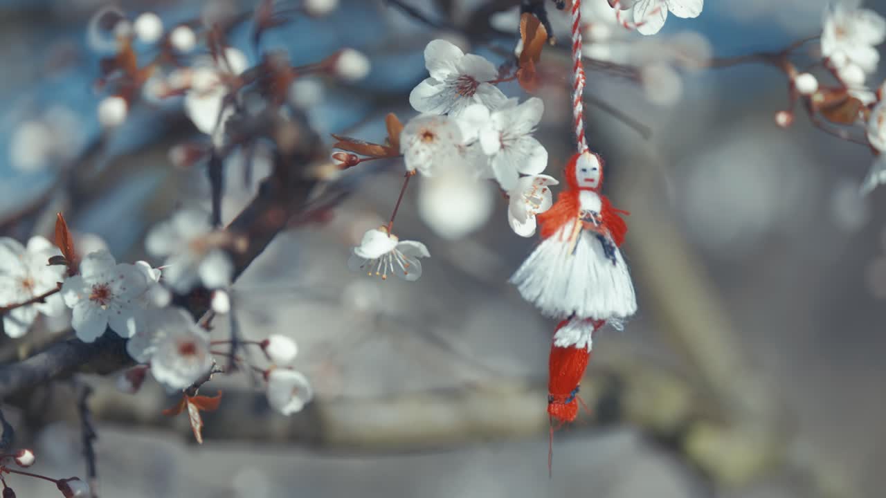 Traditional rag doll hanging from a blossoming tree branch with white flowers.