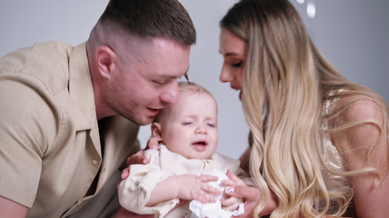 Caucasian parents kiss their adorable baby. Beautiful family of three portrait in studio. Close up.