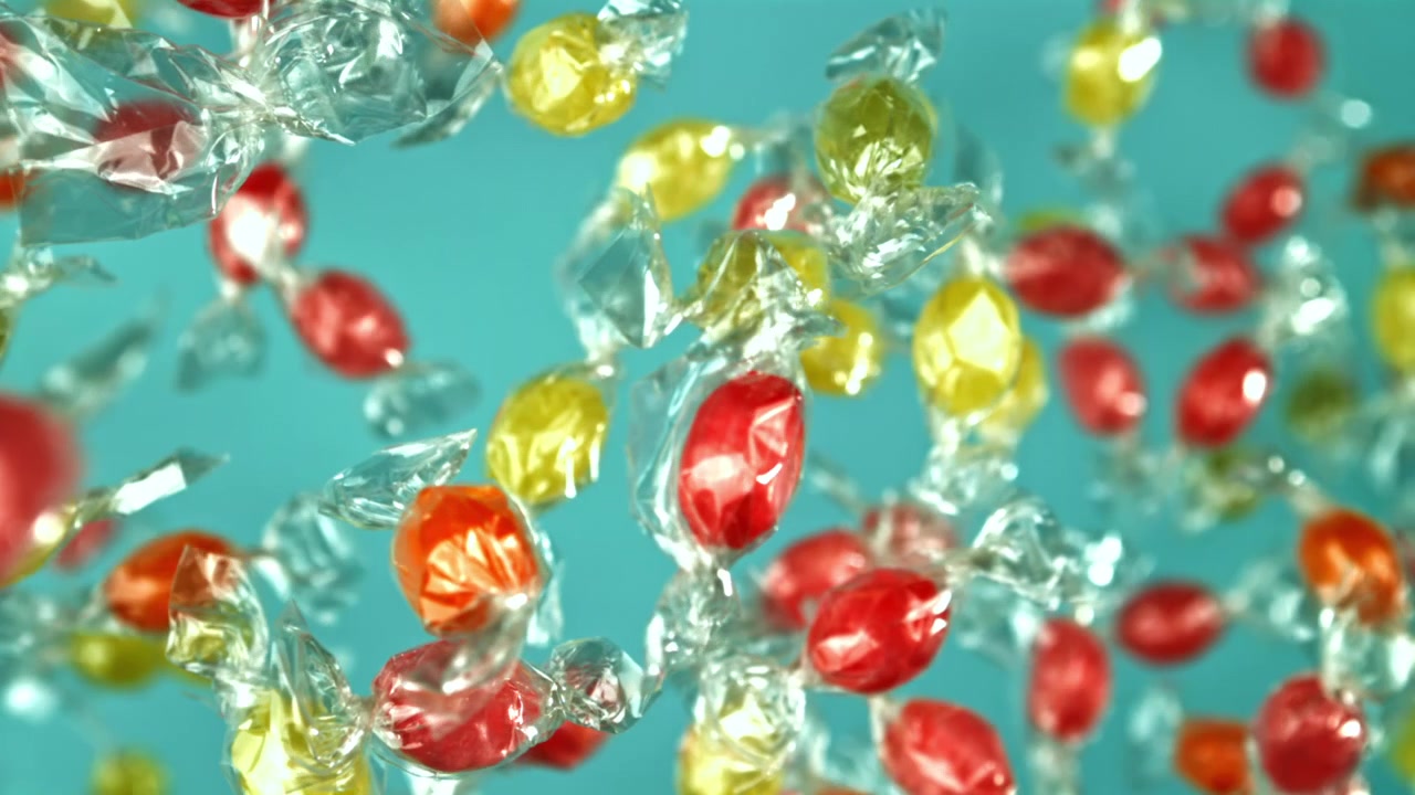 Caramelle incartate colorate che cadono al rallentatore su sfondo blu