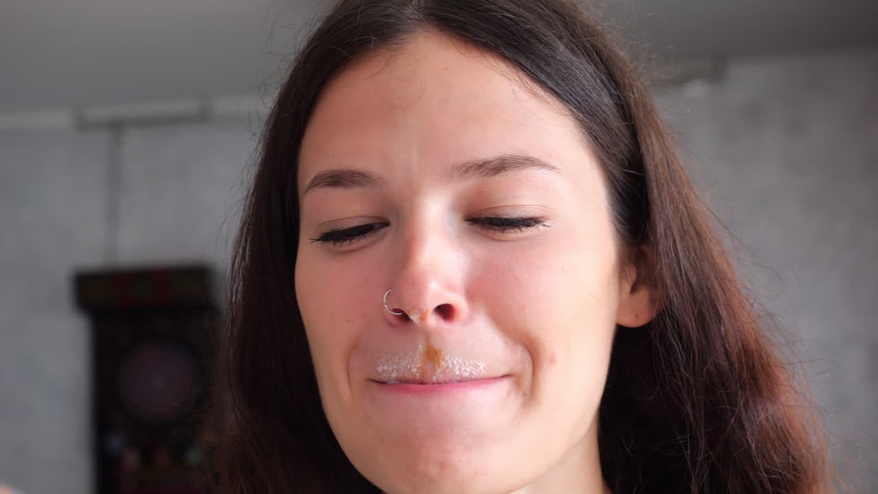 Close-up portrait captures a woman sipping espresso drink with milk foam mustache, delicately wiping her upper lip with a napkin in a casual, intimate moment