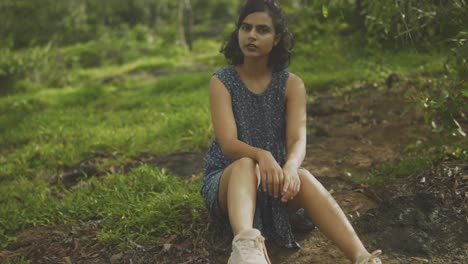 Indian-woman-sitting-on-grassy-hill-in-cute-blue-dress-gazes-with-wonder