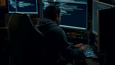 person typing on a computer with multiple screens displaying code in a dark room