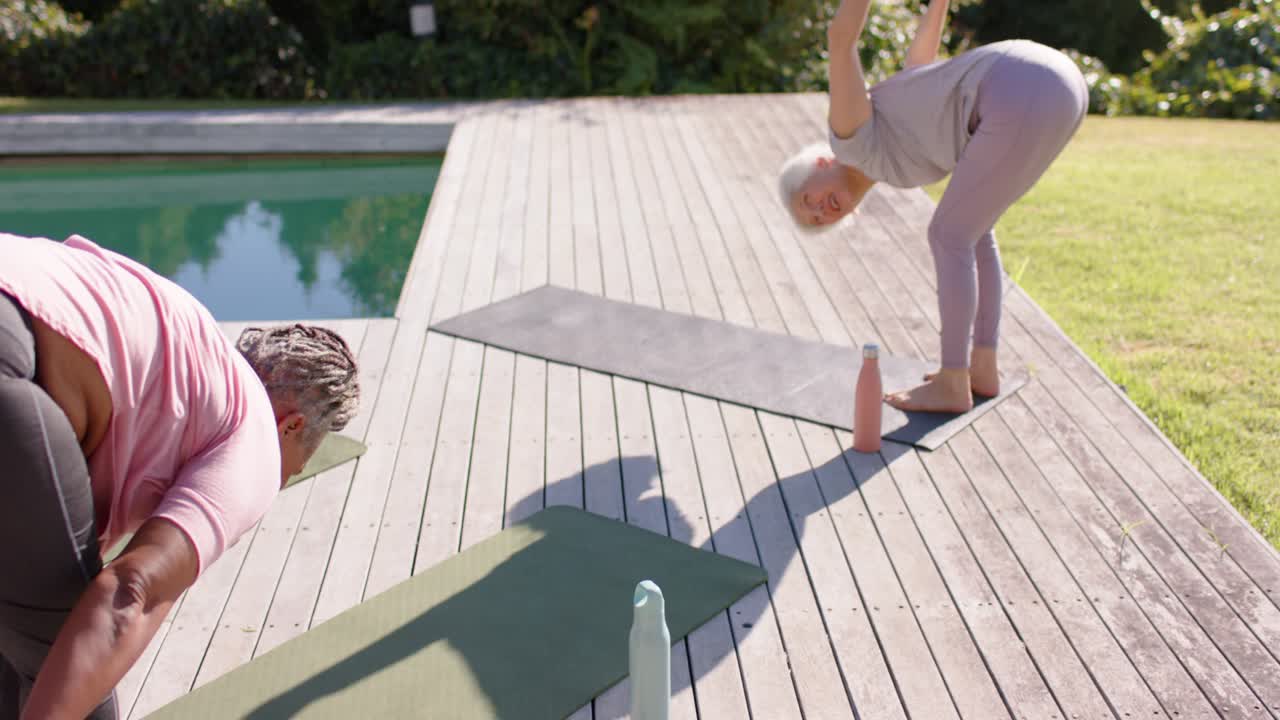 Senior diverse women holding folds on pool deck with mats,bottles after third lifting arms for yoga