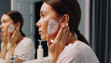 woman applies face mask in bathroom mirror