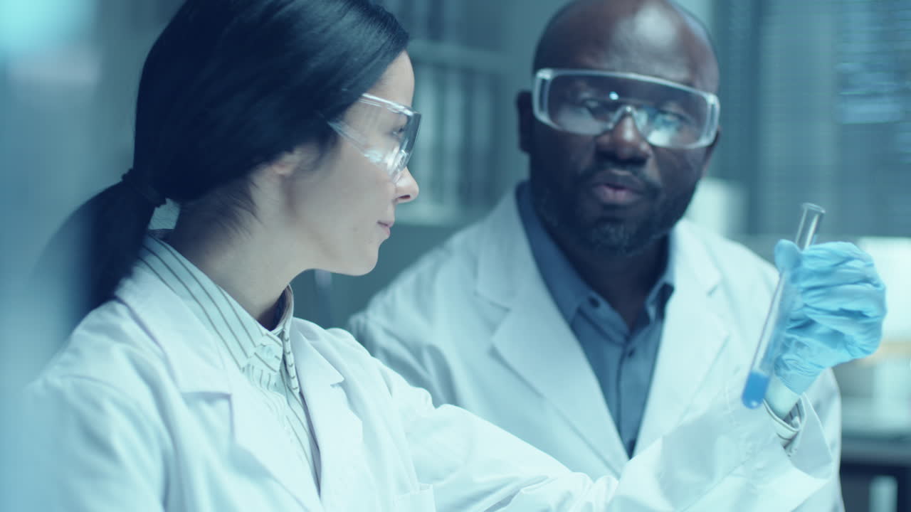 Female Chemist Discussing Liquid in Test Tube with Colleague in Laboratory