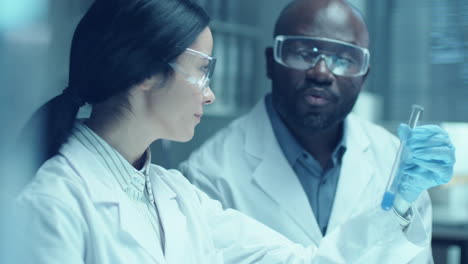 female chemist discussing liquid in test tube with colleague in laboratory