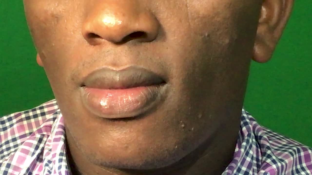 Close up shot of dark skinned man smiling into camera. Green screen in background. Macro view.