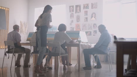 side view of a happy senior people smiling while drawing as a recreational activity or therapy in paint class together with the group of retired women and men