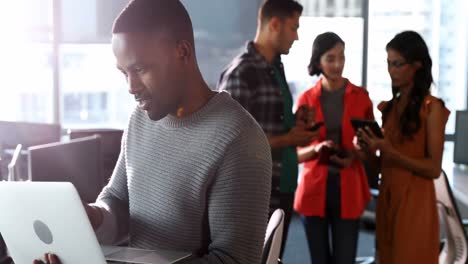 Male-executive-using-laptop-while-colleagues-using-digital-tablet-4k