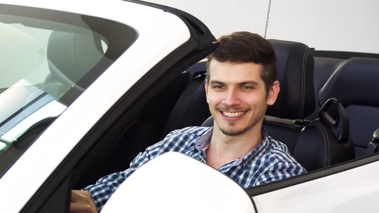 apuesto joven conductor feliz sosteniendo las llaves del coche sentado en su auto