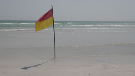 toma estática de la bandera de seguridad roja amarilla en un día ventoso en la playa del océano ondeando en el viento debido a las fuertes corrientes en el agua