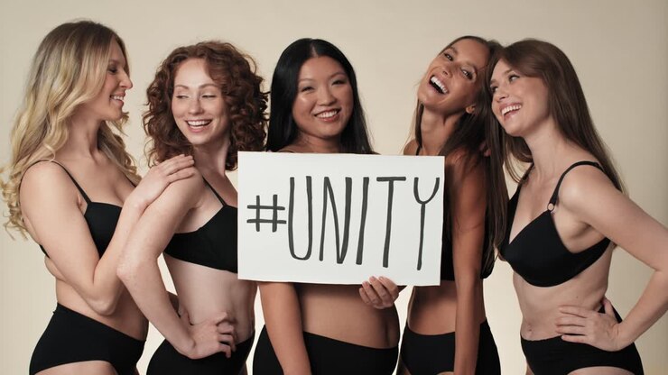 Ritratto di gruppo di donne allegre in intimo, in piedi nello studio e che tengono uno striscione.