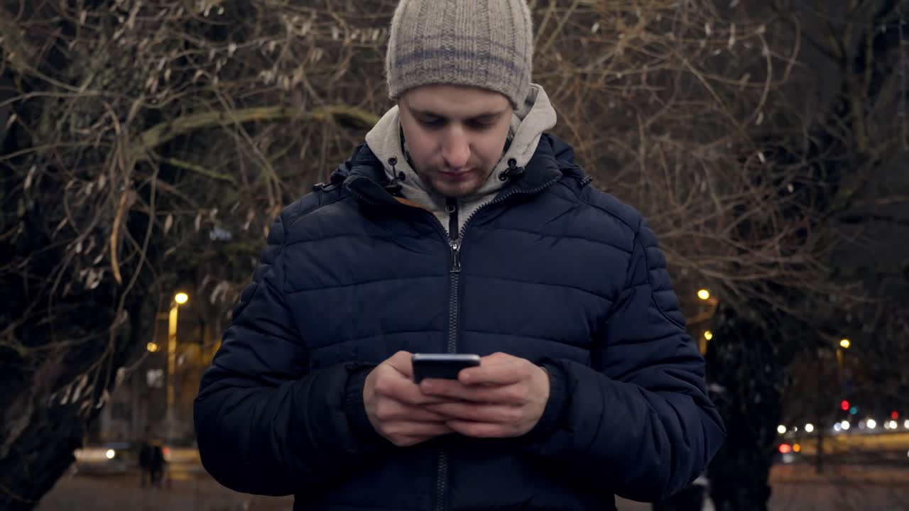 Primo piano di un uomo che digita sul suo cellulare al rallentatore mentre scuote la testa per strada.