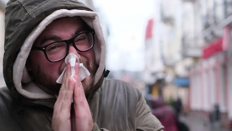 A Young Man with a Cold in the Middle of a City Street. A young man with a cold in the middle of a city street. Runny nose during the flu. Viral infections