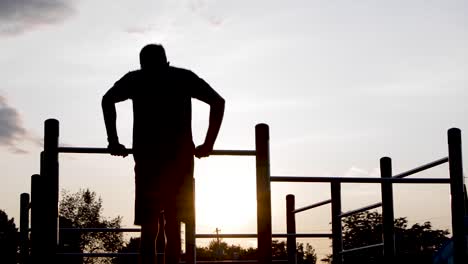 young male does flip on bar and exercising dips with bright sunrise