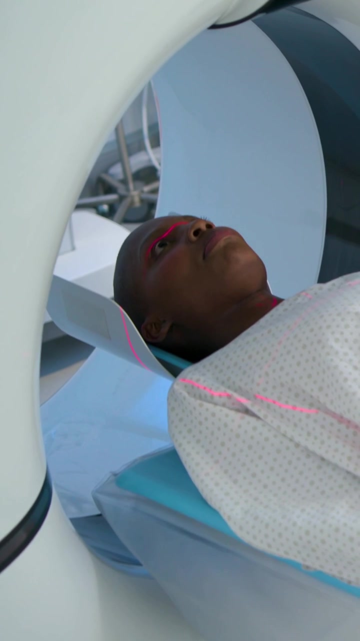 Video verticale: Tavolo in movimento, tecnico che posiziona il paziente in camice in radiologia allineando i laser per la scansione.