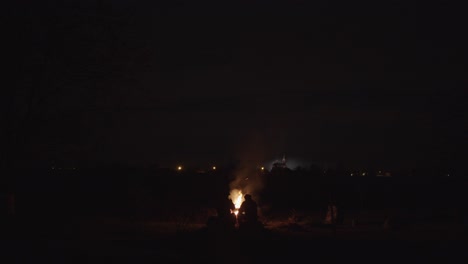 men sitting aroundsparkling  campfire dark night, center