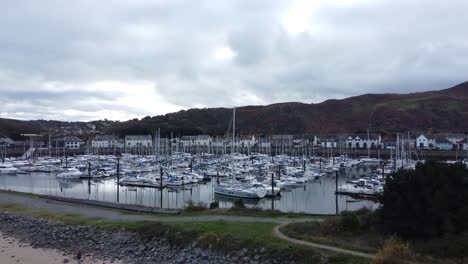 Scenic-luxurious-waterfront-harbour-apartment-village-yachts-and-sailboats-under-mountain-coastline-aerial-view-rising-over-sand-bank