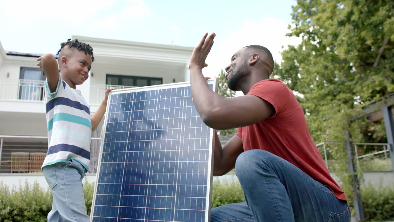padre y hijo afroamericanos high-five al lado de un panel solar al aire libre, en casa