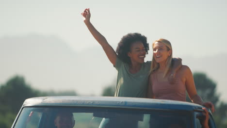 dos mujeres de pie en la parte trasera de la camioneta como amigos disfrutan de un viaje por carretera a la cabaña del campo
