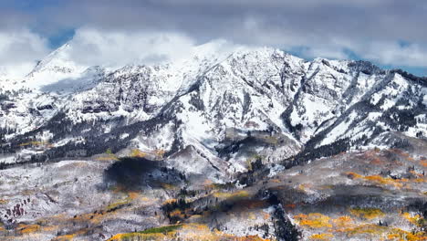 kebler pass aerial cinematic drone afternoon crested butte gunnison colorado seasons collide early fall aspen tree red yellow orange forest winter first snow powder rocky mountain peak back movement