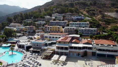 drone flies over a resort in greece crete with many houses on a beach and pool area