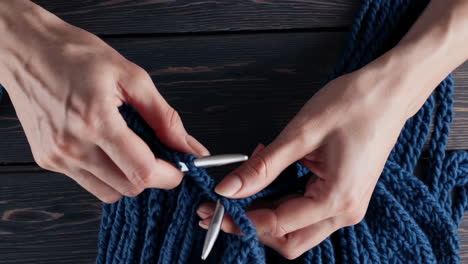 close-up of hands knitting a blue fabric with needles
