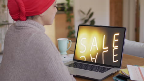 biracial woman at table using laptop, shopping online during sale, slow motion