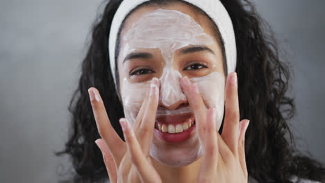 retrato de una mujer de raza mixta sonriente aplicando crema facial en el baño