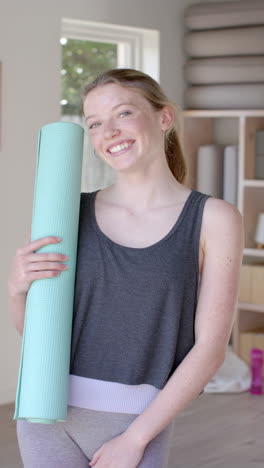 vertical video of portrait of happy caucasian woman holding mat, slow motion