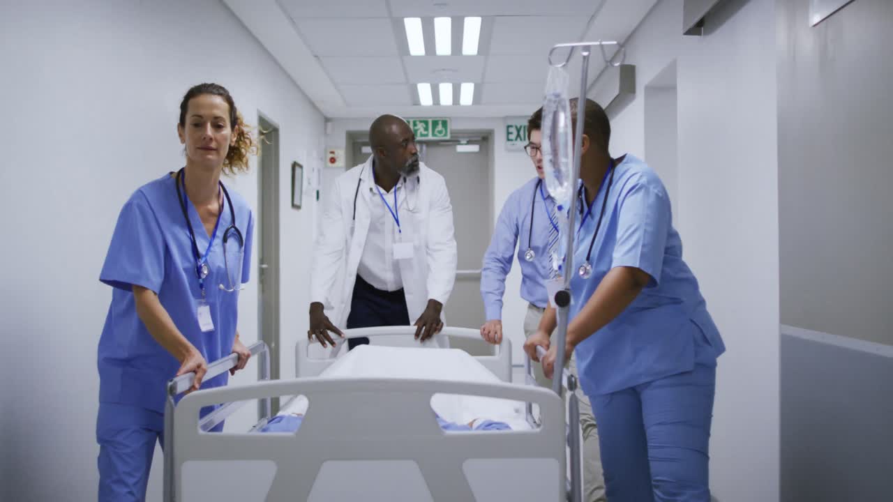 Gruppo eterogeneo di medici e dottoresse che spingono un letto in un corridoio d'ospedale e parlano.