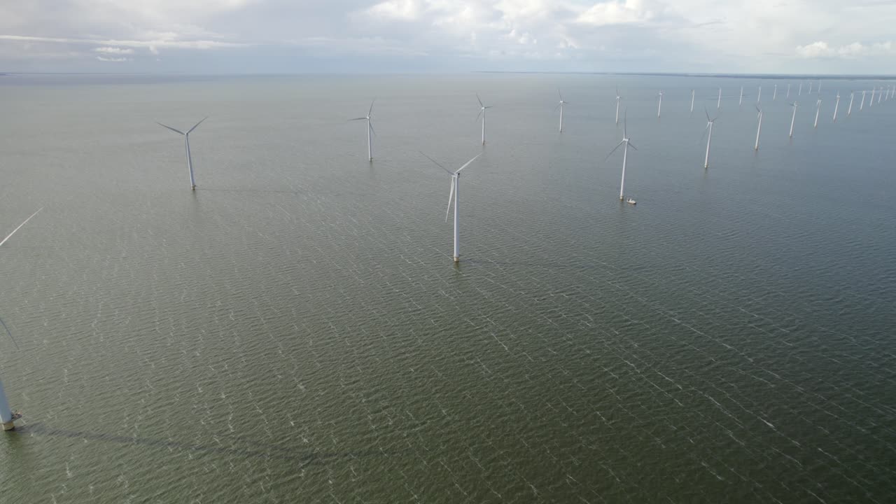 From above, an offshore wind farm stretches across the water, each turbine spinning steadily in sync.