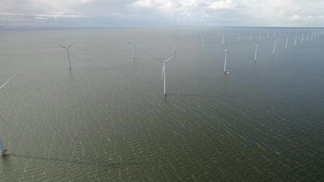 from above, an offshore wind farm stretches across the water, each turbine spinning steadily in sync.