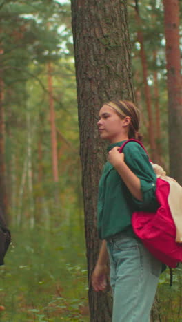 en un bosque sereno, una joven con una mochila roja ayuda a su amiga con una bufanda azul a ajustar su bolsa negra, comparten un momento cálido, sonriéndose el uno al otro, antes de continuar su caminata