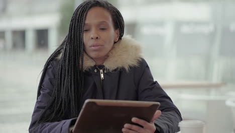 Afro-American-young-girl-with-braids-in-grey-jacket-with-fur-hood-sitting-outside