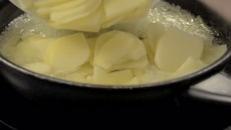 verter patatas picadas en rodajas en una sartén con cebollas cortadas