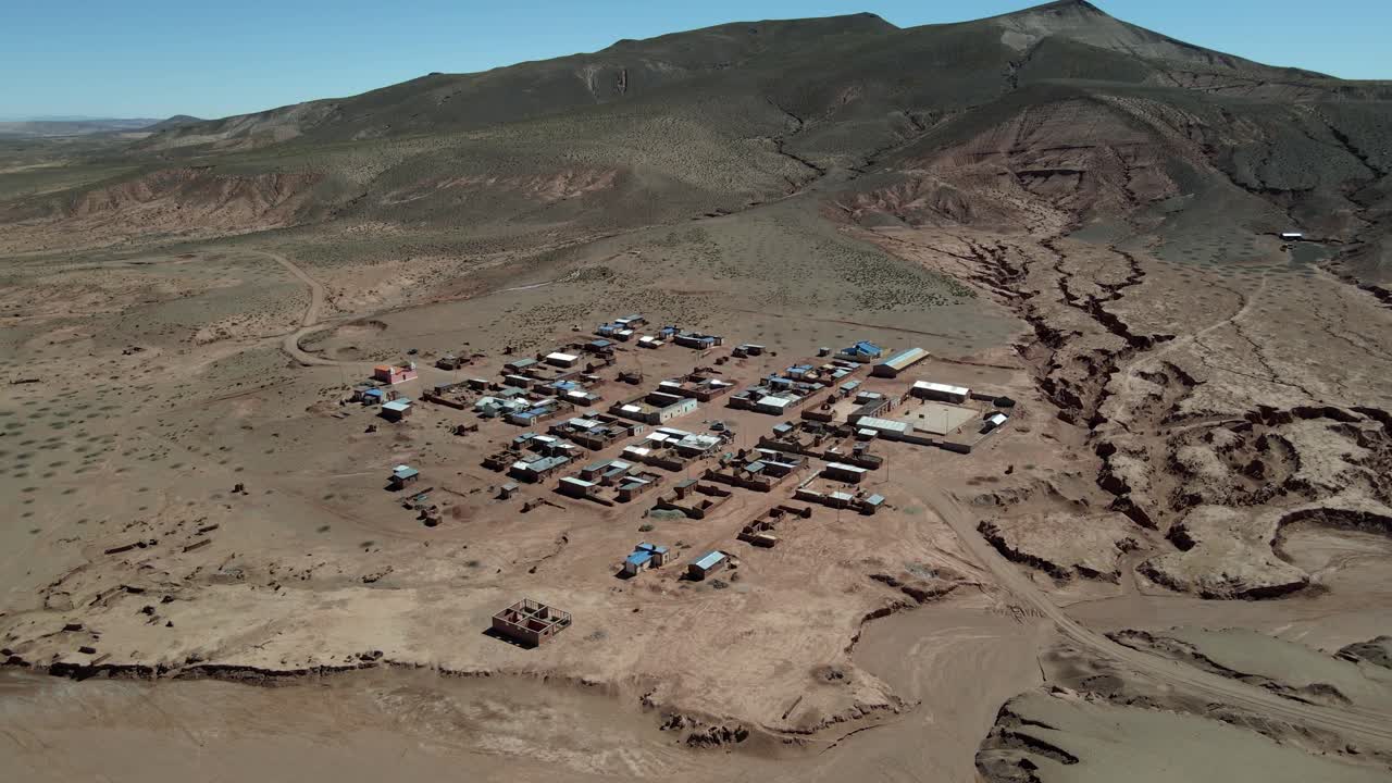 Drone flies above remote Bolivian village showing homes in sparse highland desert landscape