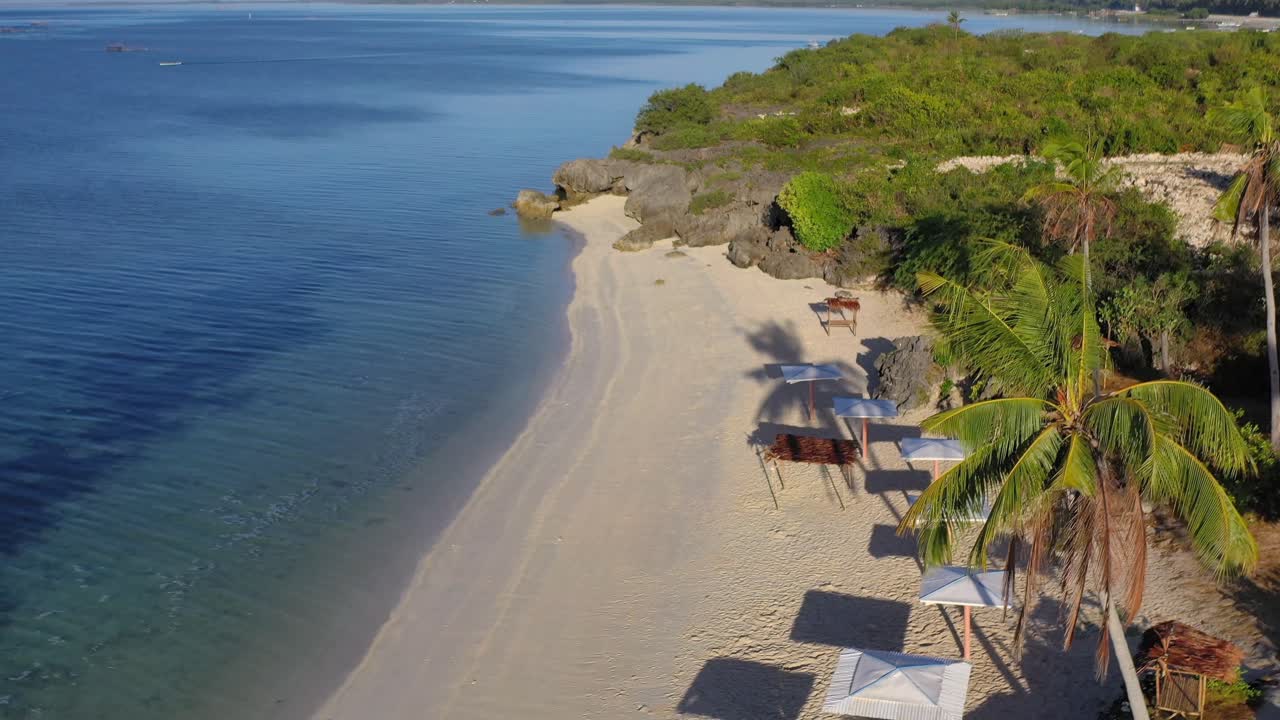 Beautiful beach at Hilantagaan island Philippines with sun umbrellas and rocky shore, Aerial dolly in shot
