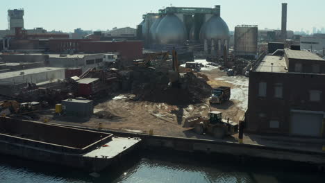 Slide-and-pan-aerial-shot-of-truck-arriving-on-loose-material-dump.-Loading-material-on-barge.-New-York-City,-USA