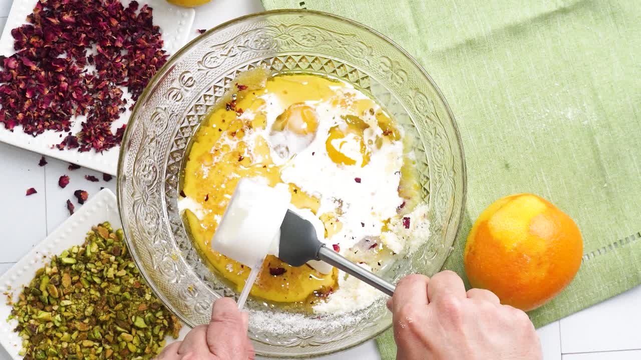Baking a dessert called Persian Love Cake made with rose petals and pistachios. Cake with white glaze frosting. Mixing in the sour cream to the batter. Beautiful cake for tea time or celebration