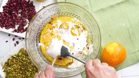 baking a dessert called persian love cake made with rose petals and pistachios. cake with white glaze frosting. mixing in the sour cream to the batter. beautiful cake for tea time or celebration