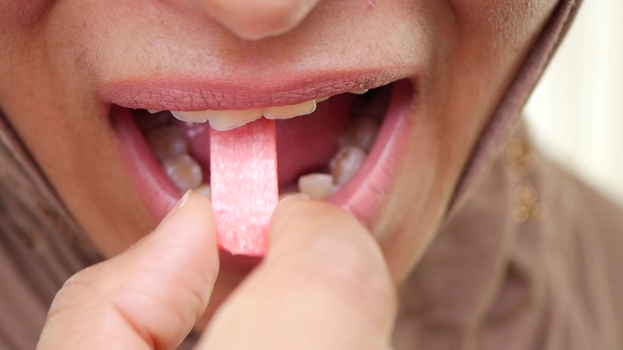 Primo piano di una donna che mette un pezzo di gomma da masticare in bocca