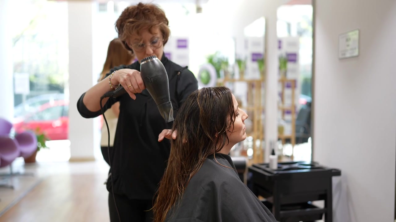 Parrucchiere professionista che asciuga i capelli di una cliente con il phon in un salone