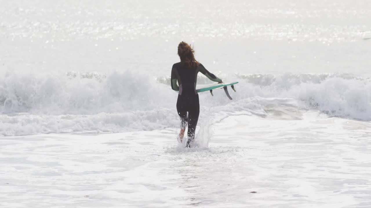 서프 보드를 들고 바다로 달리는 혼합 인종 여성의 뒷면