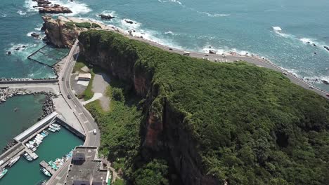 Cinematic-Aerial-of-Coastal-Road-Around-Steep-Limestone-Cliffs-With-Rainforest-and-Pier-in-North-Taiwan,-Yehliu-Geopark