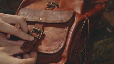 woman's hands opening the pocket belt buckle of a leather retro brown backpack - closeup shot